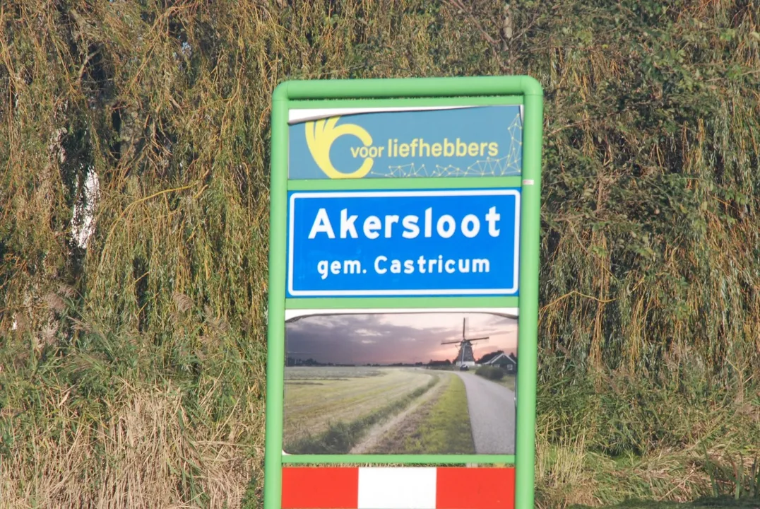 Signpost with blue Akersloot sign reading 'Akersloot gem. Castricum' and a windmill landscape below, in a green frame